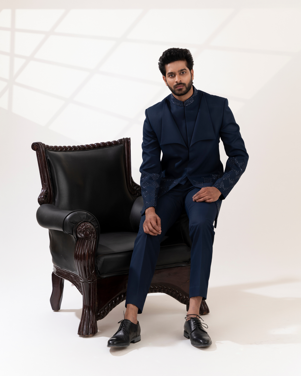 Man in a navy suit sitting on a black leather armchair 