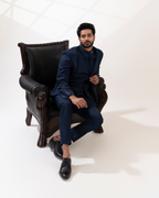 Man in a navy blue outfit sitting on a dark leather armchair