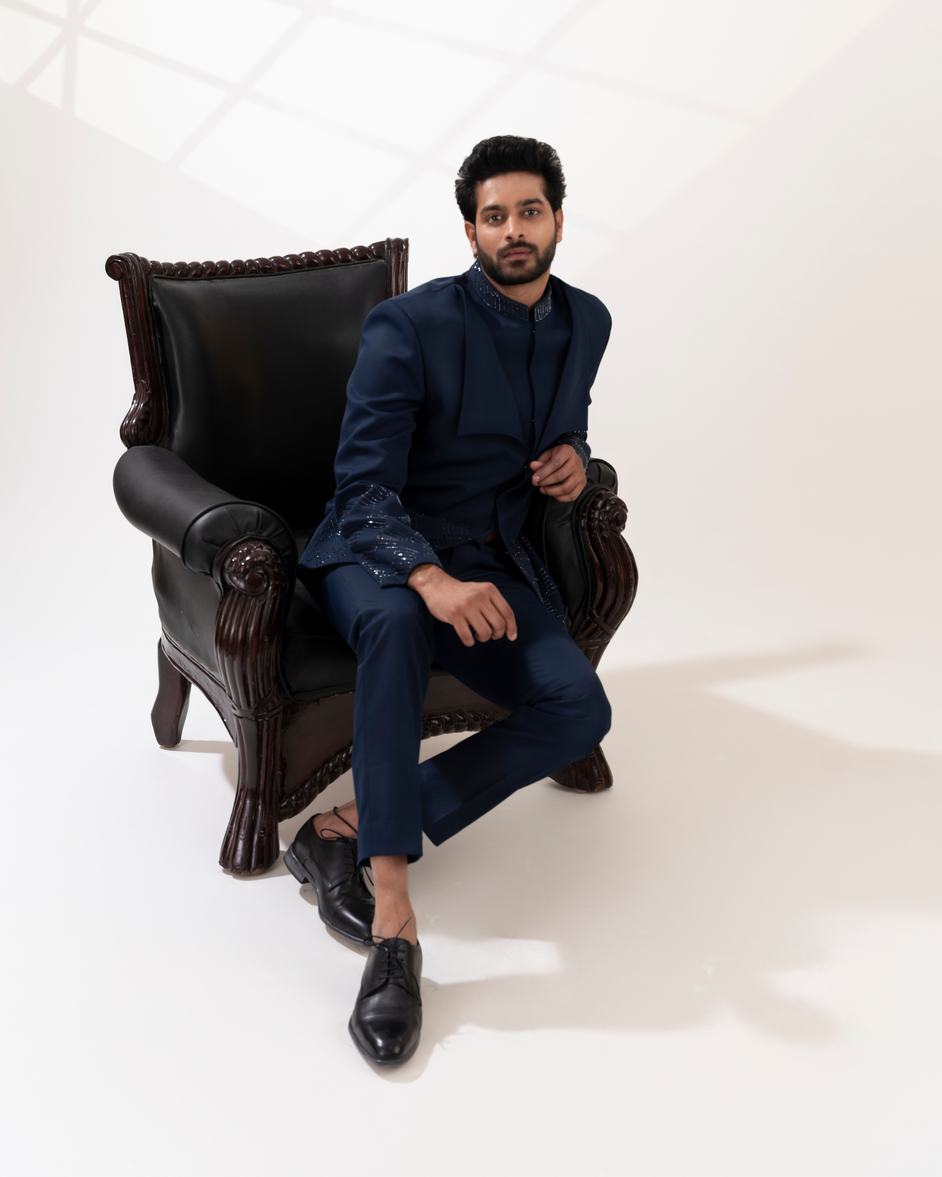 Man in a navy blue outfit sitting on a dark leather armchair