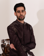 Man wearing a dark brown traditional outfit with intricate foliage embroidery pattern