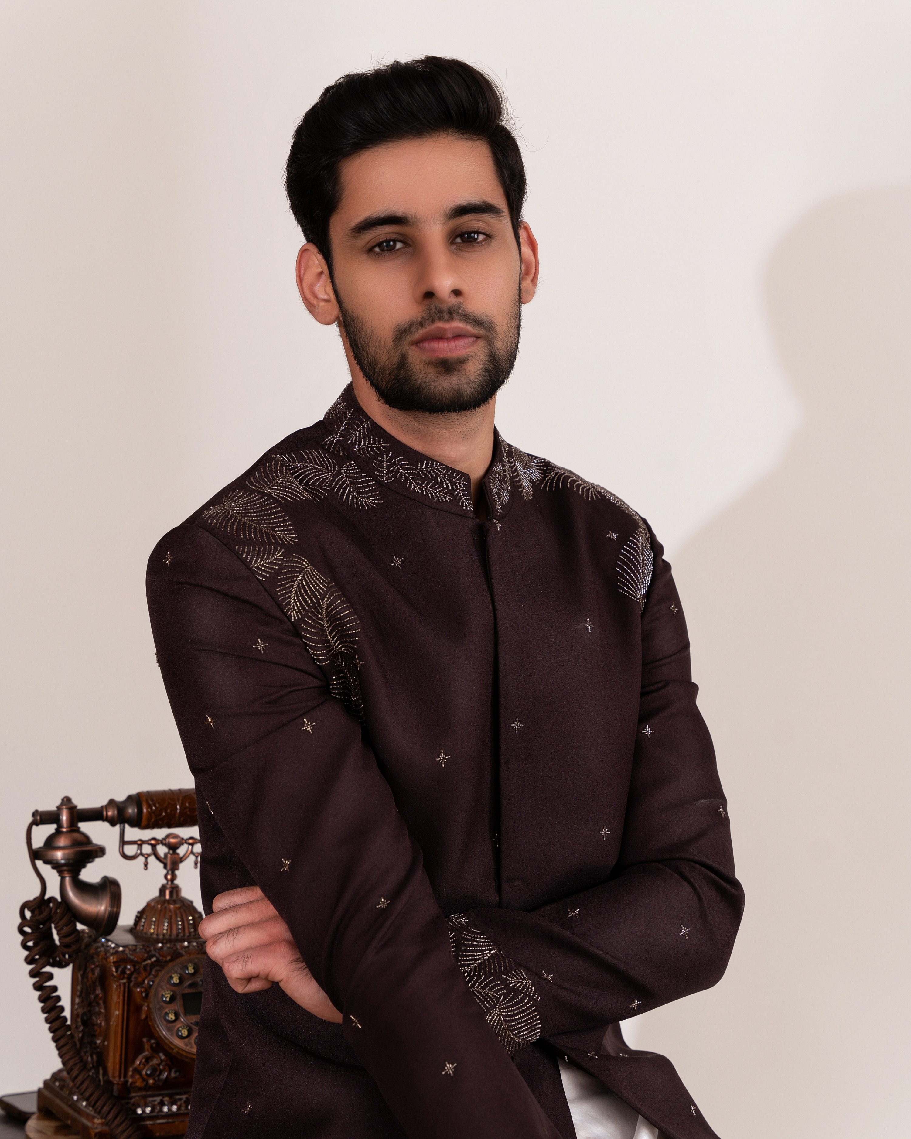 Man wearing a dark brown traditional outfit with intricate foliage embroidery pattern