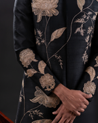 Macro shot showing intricate gold thread embroidery on black sherwani