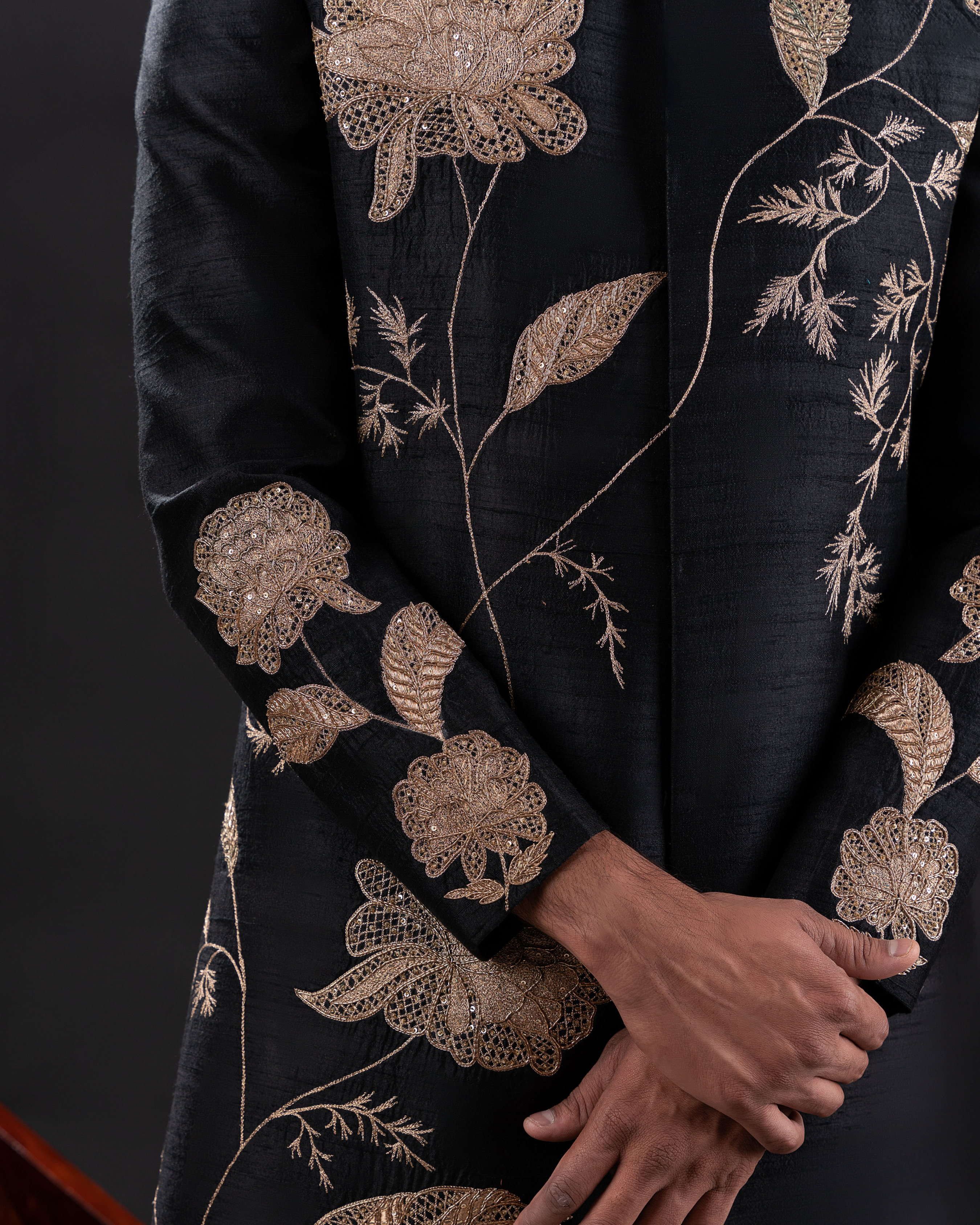 Macro shot showing intricate gold thread embroidery on black sherwani