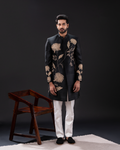 Front view of a black sherwani with golden floral embroidery and white pants