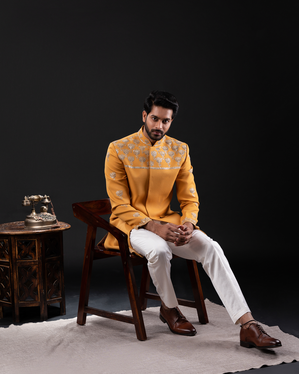 Front view of yellow embroidered bandhgala jacket and white pants sitting on a wooden chair 