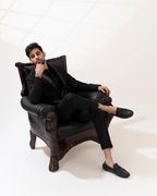 Man in black suit sitting on a black leather armchair against a white background