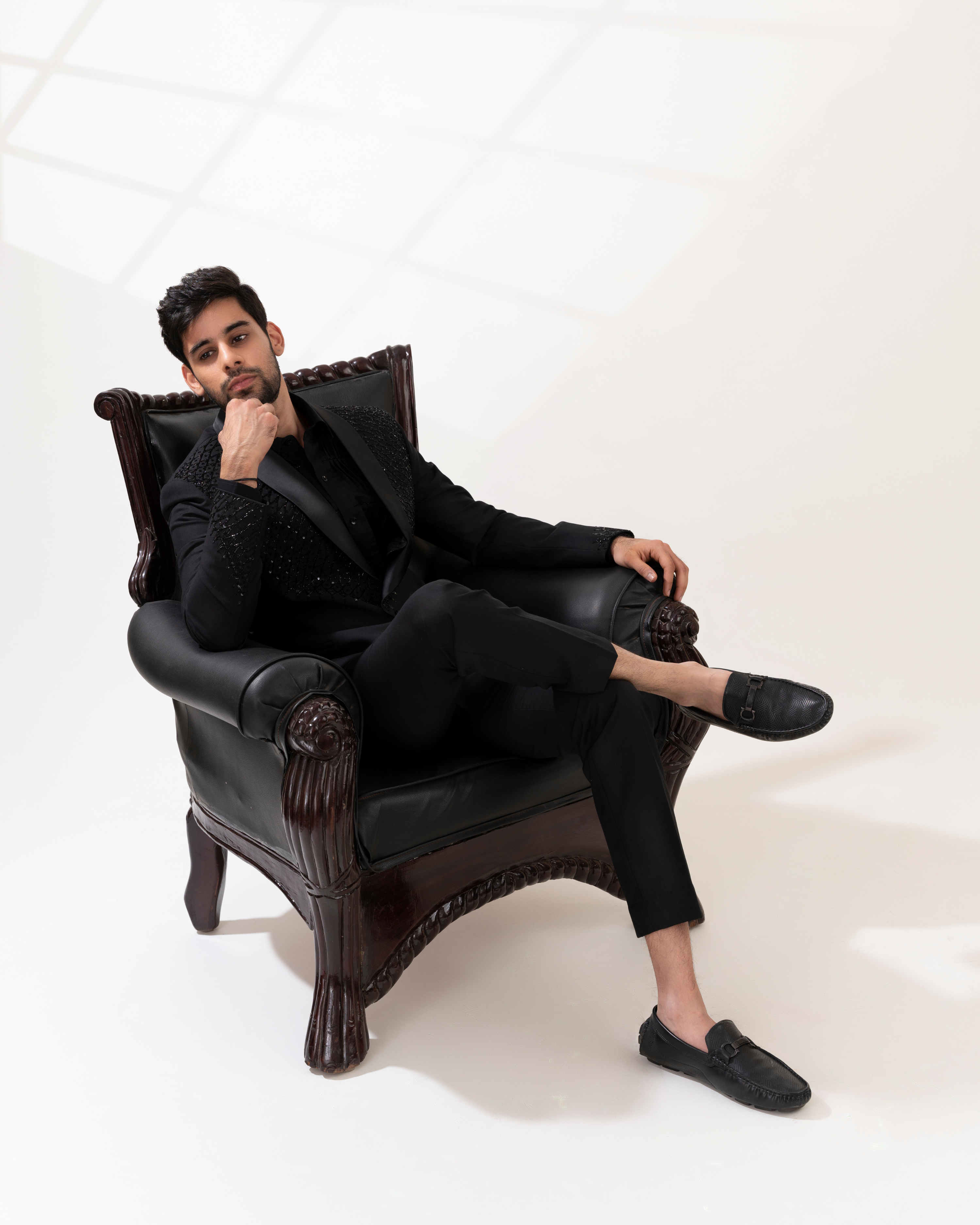 Man in black suit sitting on a black leather armchair against a white background